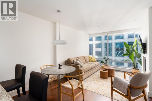 Dining area with wooden chairs and table, adjacent to living room and kitchen with city views. - 2704 1111 Alberni Street, Vancouver