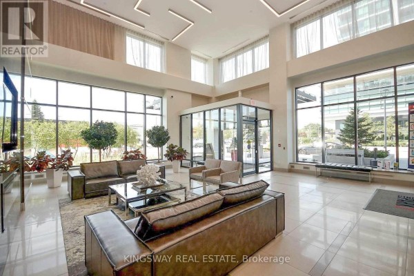 Spacious building lobby with beige sofas, glass tables, and large windows. - 2706 - 3975 Grand Park Drive, Mississauga