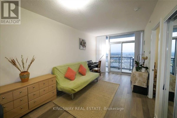 Apartment living area with green sofa, piano, dresser, and city view balcony. - 2706 - 3975 Grand Park Drive, Mississauga
