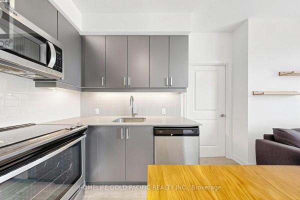 Open-concept kitchen and living area with grey cabinets, a wooden island, and a grey sectional sofa. - 2708 - 8 Nahani Way, Mississauga