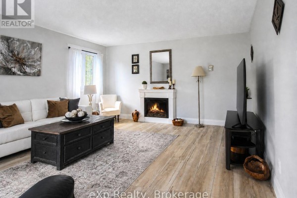 Living room with light wood floors, white sofa, fireplace, television, and a dark wood coffee table. - 271 River Road, Grey Highlands