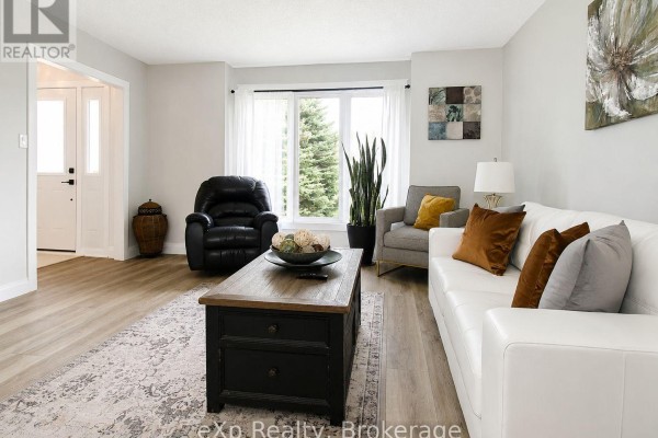 Living room with light wood floors, white sofa, black leather recliner, and a dark wood coffee table and entrance hall. - 271 River Road, Grey Highlands