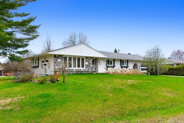 Side view of a white house with stone and stone tile exterior accents and a lawn. - 271 Rue Leguerrier O., Mansfield Et Pontefract