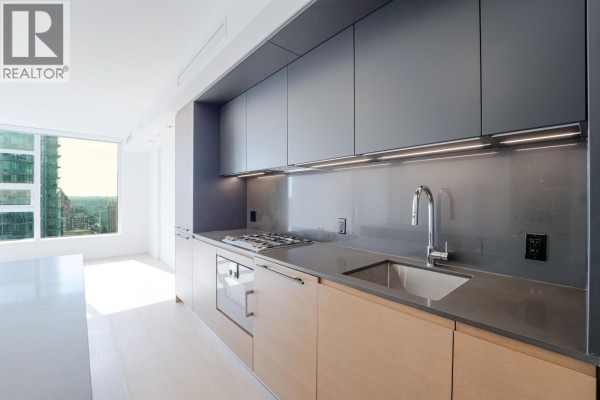 Staged modern kitchen and living area with island, sofa, and city view. - 2710 1289 Hornby Street, Vancouver