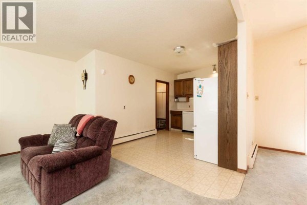 Living room and kitchen area with a recliner, refrigerator, and wood cabinets. - 2710 6a Avenue N, Lethbridge
