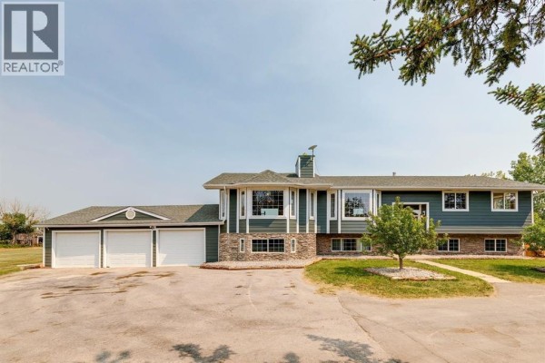 Front view of a dark green house with stone accents, multiple windows, and a paved driveway with a three-car garage. - 271154 Range Road 285, Rural Rocky View County