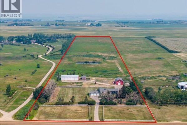 Aerial view showing a property boundary encompassing a house, multiple outbuildings, and fenced fields within a larger landscape. - 271154 Range Road 285, Rural Rocky View County