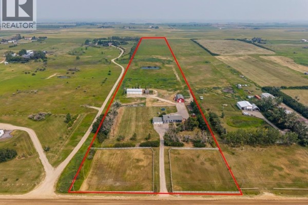 Aerial view of the property with a red boundary line highlighting the house, outbuildings, fields, and surrounding agricultural land. - 271154 Range Road 285, Rural Rocky View County