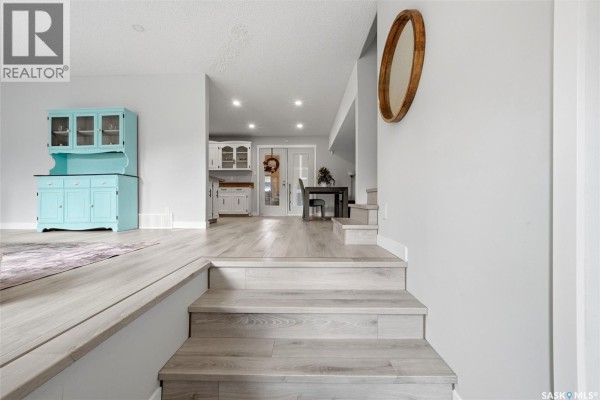 Interior view showing light wood laminate flooring and stairs leading to a kitchen and dining area. - 2714 Jaques Place E, Regina