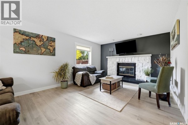 Living room featuring a stone fireplace, dark sofa, green accent chair, and a world map wall art. - 2714 Jaques Place E, Regina