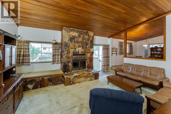 Living room featuring a large stone fireplace, wood ceiling, and beige carpet. - 2715 Wildwood Crescent, Prince George