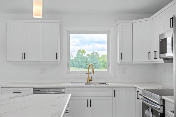 Kitchen sink with gold faucet below a wide window overlooking trees. - 272 Fernwood Way, New Bothwell