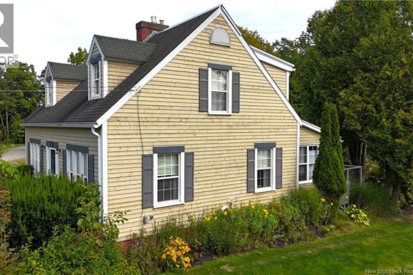 Side view of the light yellow house with horizontal siding, dark shutters, and landscaped garden. - 272 Milltown Boulevard, St  Stephen