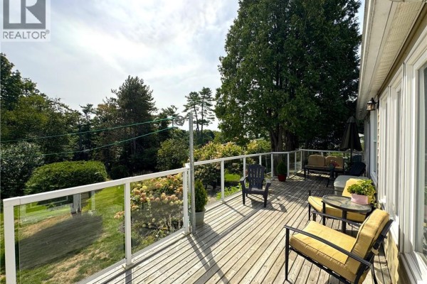 Wooden deck with glass railings overlooking a green lawn and mature trees on a sunny day. - 272 Milltown Boulevard, St  Stephen