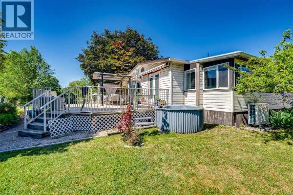 Rear exterior of mobile home with a covered deck, hot tub, and grassy yard. - 2727 Lakeshore Road Unit# 106, Vernon