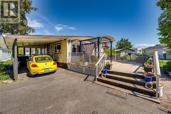 A small creek flows through a grassy field with trees and distant hills. - 2727 Lakeshore Road Unit# 106, Vernon