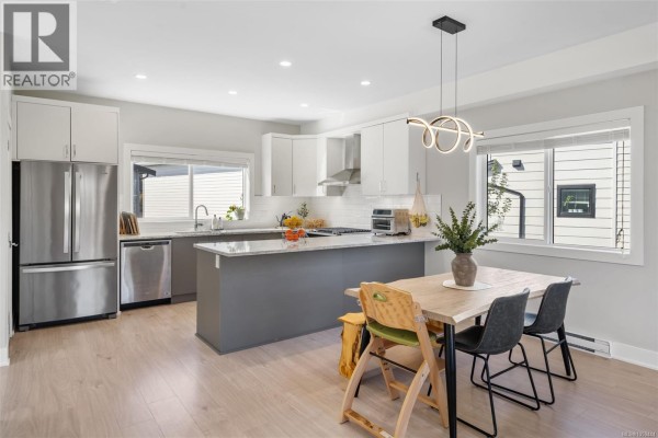 Open concept kitchen and dining area with a grey island, white cabinets, and wood flooring. - 2728 Celestial Crt, Langford