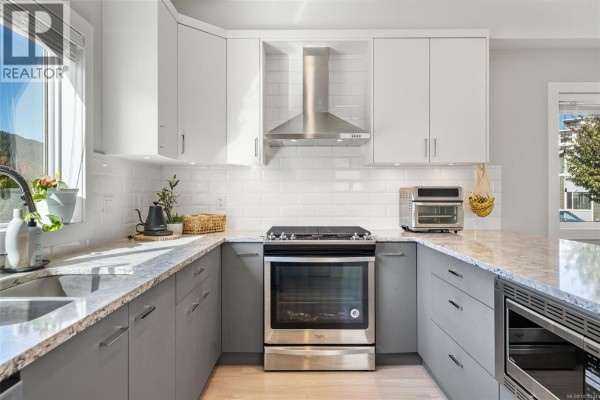 U-shaped kitchen with grey lower cabinets, white subway tile backsplash, and granite countertops. - 2728 Celestial Crt, Langford
