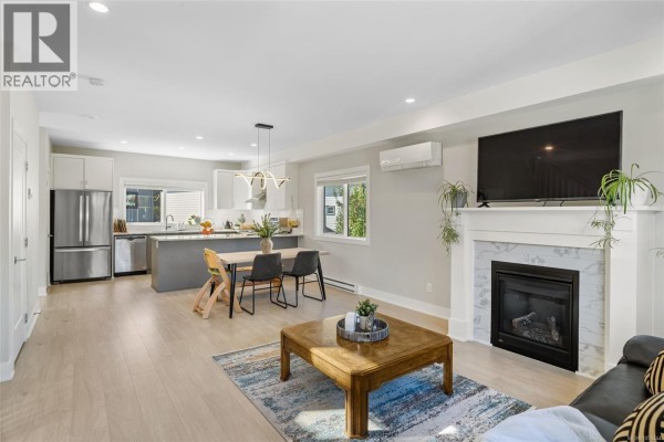 Living room with a gas fireplace, large sofa, coffee table, and view of the open kitchen. - 2728 Celestial Crt, Langford