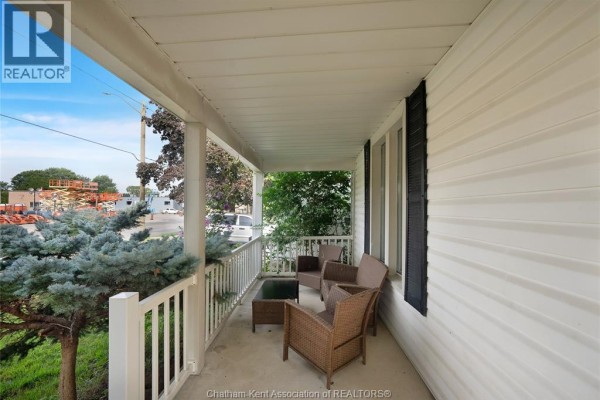 Covered front porch with white railings and seating area overlooking the street. - 273 St Clair Street, Chatham