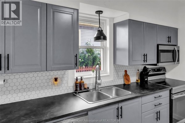 Kitchen sink with a double basin, grey cabinets, and a white hexagonal tile backsplash. - 273 St Clair Street, Chatham
