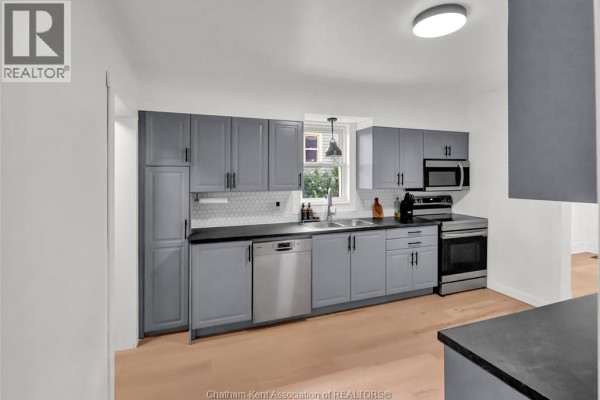 A view of the grey-paneled kitchen with stainless steel appliances and a window above the sink. - 273 St Clair Street, Chatham