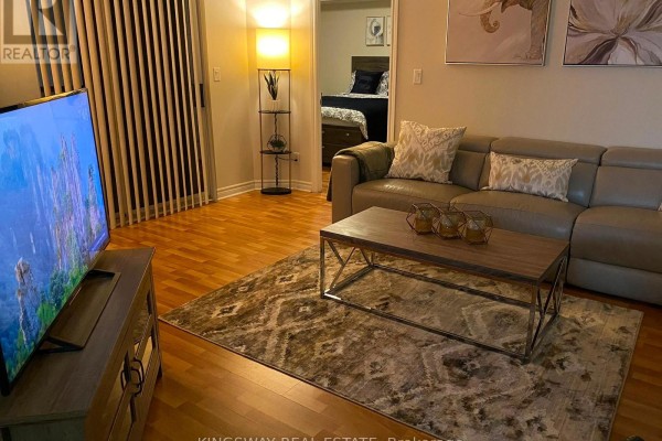 Living room with grey leather sectional sofa, wood coffee table, patterned rug, and television. - 2730 - 3888 Duke Of York Boulevard, Mississauga
