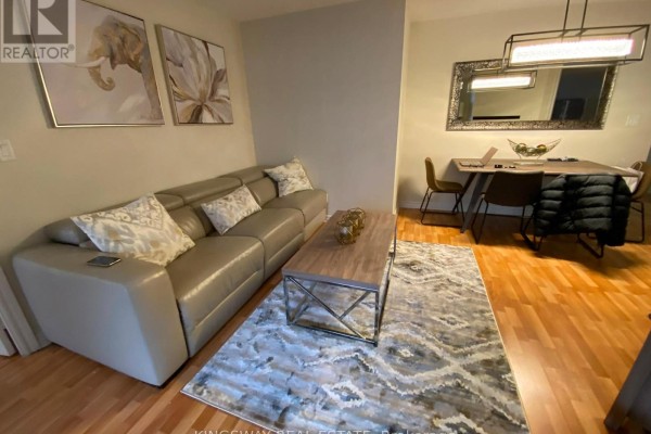 Living room with light grey sofa and patterned rug, adjacent to dining area with rectangular table. - 2730 - 3888 Duke Of York Boulevard, Mississauga