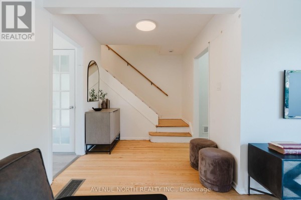 Interior entryway with light wood floors, a staircase with white risers and wood handrail, and a grey console table. - 2732-2730 Colman Street, Ottawa