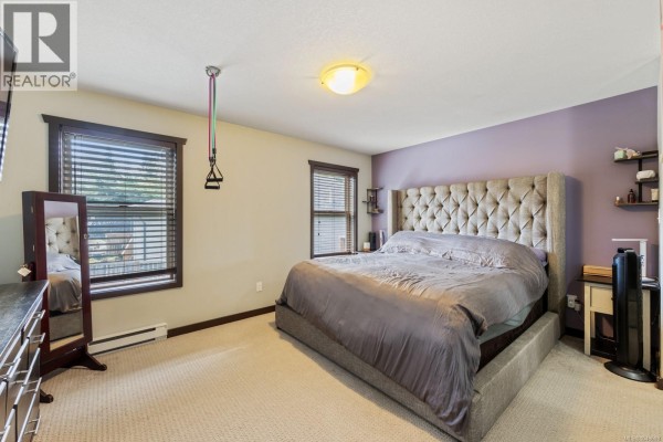 Master bedroom with a king-sized bed, purple accent wall, and large windows - 2735 Rydal Ave, Cumberland