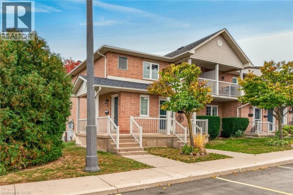 Left side exterior view of a brick townhouse with trees and a balcony. - 2737 King Street E Unit# 55, Hamilton