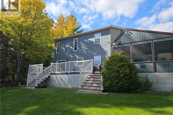 Back of a blue house with a large white deck and stairs leading to a green lawn. - 2737 Middle River Rd, Middle River