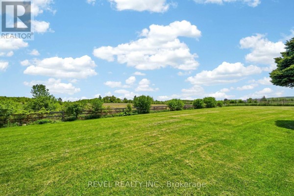 Expansive green lawn with a wooden fence and trees under a blue sky. - 2738 Lower Base Line, Milton