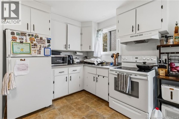 Kitchen with white cabinets, refrigerator, stove, and tiled flooring. - 275-279 Ayer, Moncton