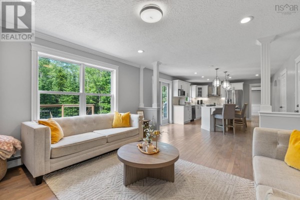 Living room with a large window overlooking trees, beige sofa, coffee table, and open access to the kitchen. - 275 Canterbury Lane, Fall River