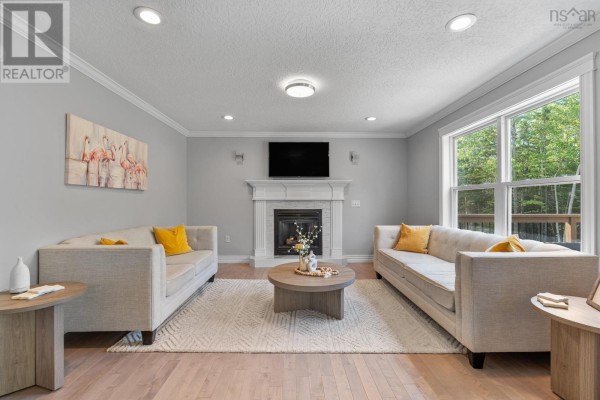Living room with two beige sofas, fireplace, coffee table, and a large window with tree views. - 275 Canterbury Lane, Fall River