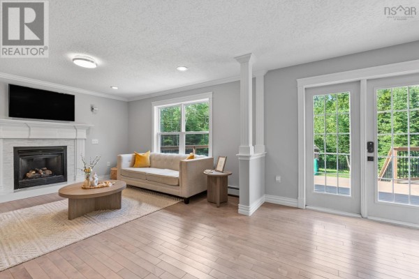 Living room with a fireplace, beige sofa, sliding glass doors leading to a deck, and wood floors. - 275 Canterbury Lane, Fall River