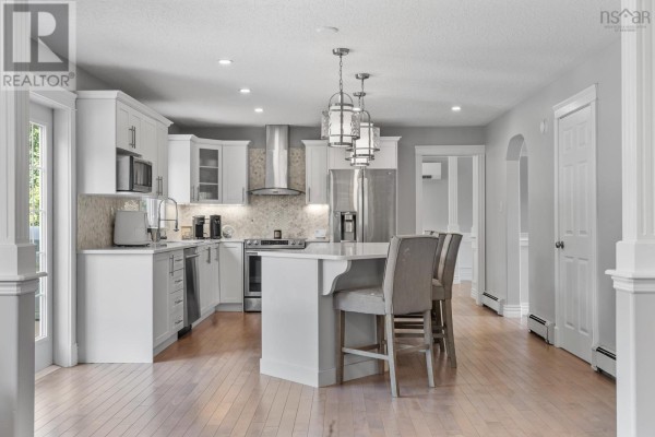 White kitchen with stainless steel appliances, island with bar stools, and pendant lighting, open to dining area. - 275 Canterbury Lane, Fall River