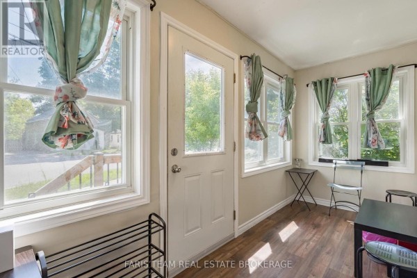 Interior of a sunlit room with large windows, floral curtains, and a white door. - 275 Gill Street, Orillia