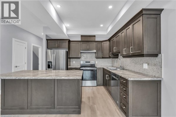 Interior hallway with light grey walls, wood-look flooring, and a wooden staircase with a dark railing. - 275 James Street S Unit# 20, St  Marys