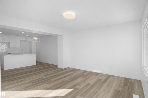Living area with light wood floors, white walls, and a partial view of the kitchen island. - 276 Deer Valley Dr, Leduc