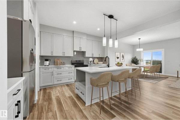 Modern kitchen with light grey cabinets, white countertops, an island with pendant lights, and stainless steel appliances. - 276 Lodge Pole Pl, Leduc