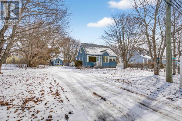 Front view of a blue house with a snow-covered driveway and trees - 276 South Drive, Summerside