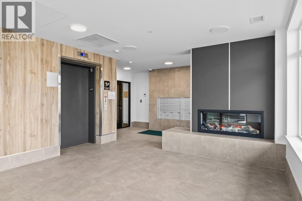 Apartment building lobby with elevator, mailboxes, modern fireplace, and large windows. - 2760 Olalla Road Unit# 506, West Kelowna