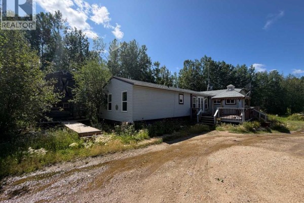 Side view of the mobile home with a wooden deck and surrounded by trees. - 2761 Bambi Street, Wabasca