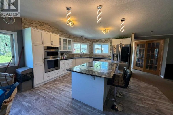 A large kitchen with white cabinets, a granite island, and stainless steel appliances. - 2761 Bambi Street, Wabasca