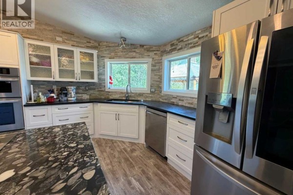 Close-up of the kitchen with white cabinets, stone backsplash, and windows. - 2761 Bambi Street, Wabasca