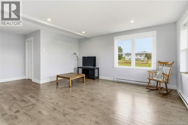 Living room with light grey walls, large window, television, coffee table, and wooden rocking chair. - 2764 Route 515, Sainte Marie De Kent