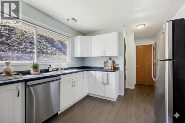 Primary bedroom with a queen bed, wooden nightstand, closet, and large window with a view. - 2768 Valleyview Drive, Kamloops