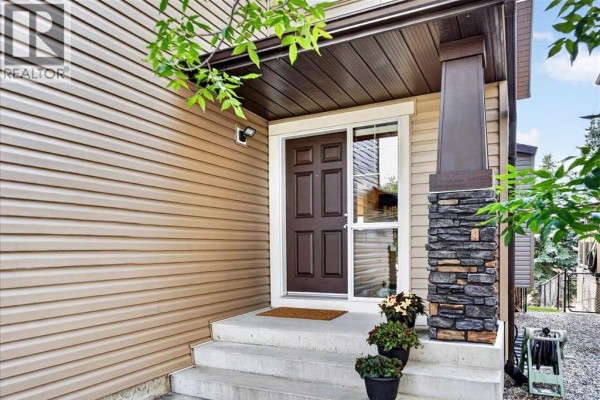 Exterior view of the front entrance with a brown door, glass side panel, and stone pillar. - 277 Evermeadow Avenue Sw, Calgary